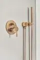 Badearmatur mit zwei Hebeln und Handbrause in brushed gold, montiert an einer glatten Wand. Ideal Standard Logo sichtbar.